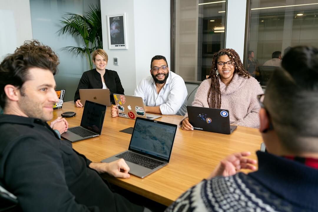 A group of people seated at a table, each using laptops, engaged in a discussion about AI knowledge management.